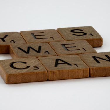 Scrabble tiles spelling 'Yes We Can' on a white background, conveying encouragement.